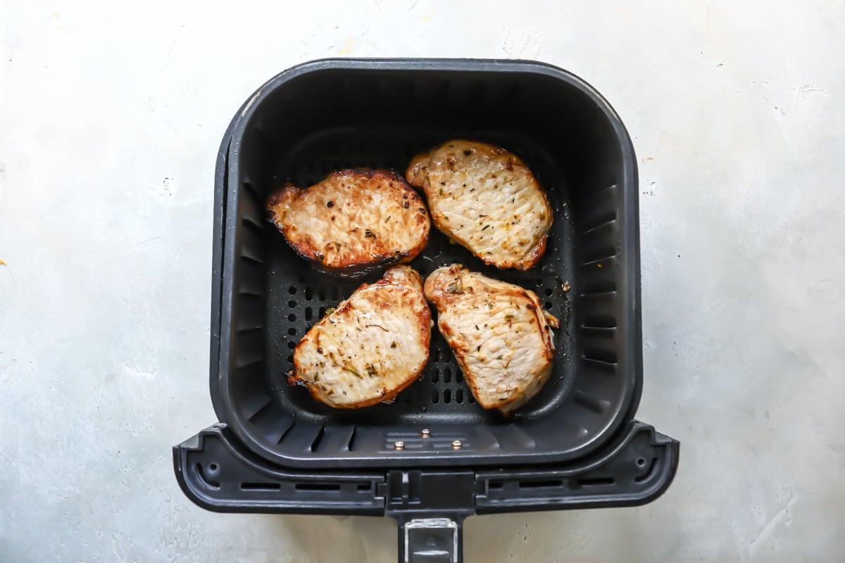 Pork chops in an air fryer basket after being air fried.