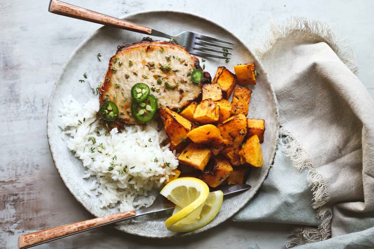 A plate with an air fryer pork chop, air fryer butternut squash, and baked rice on it.