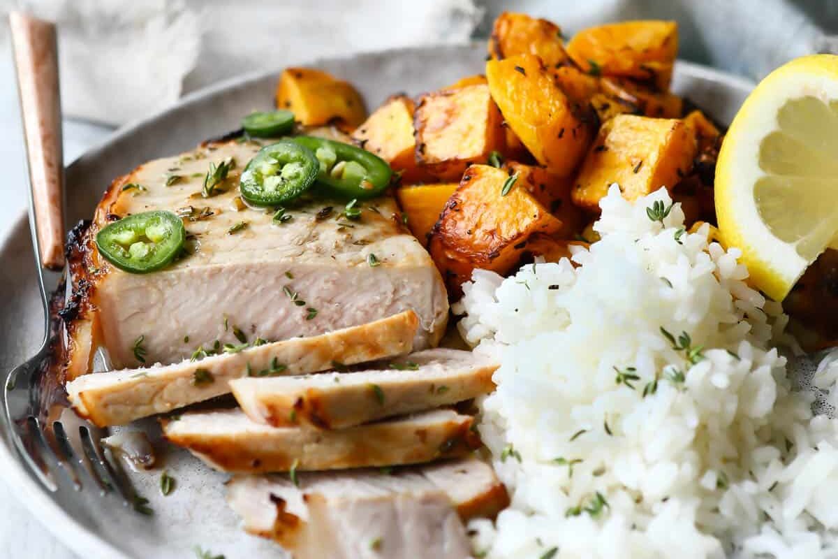 A plate with sliced air fryer pork chop, air fryer butternut squash, and baked rice on it.