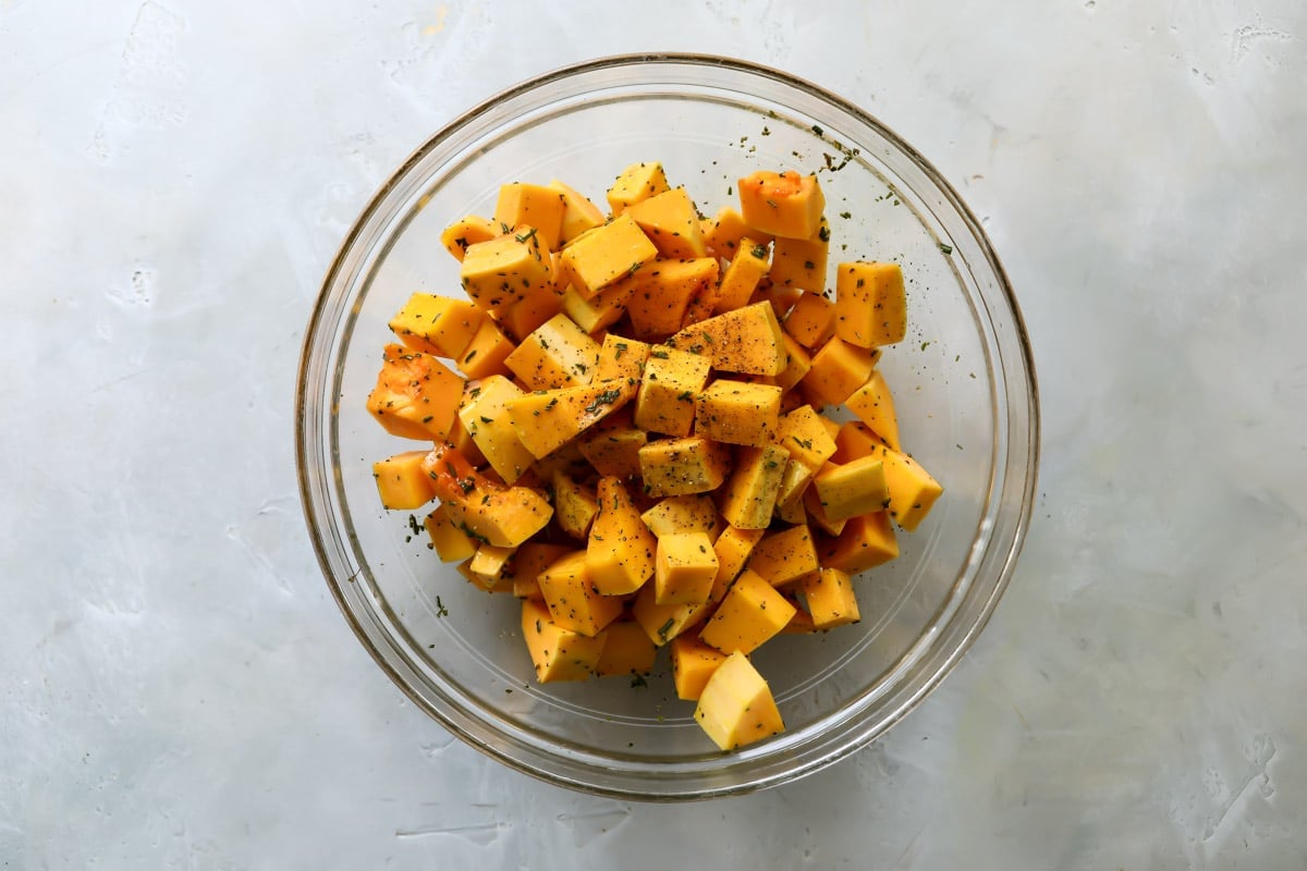 A bowl of cubed butternut squash with spices and oil.