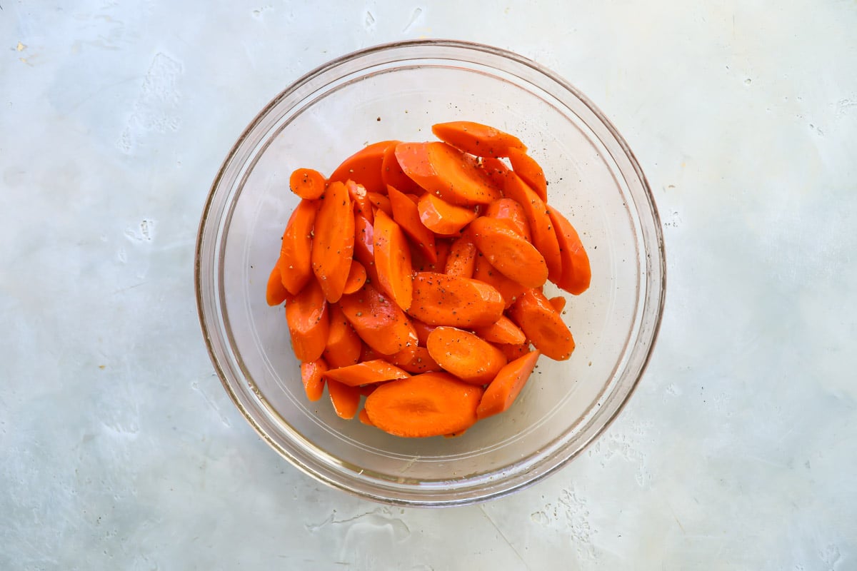 Carrots in a clear bowl with oil, salt and pepper.