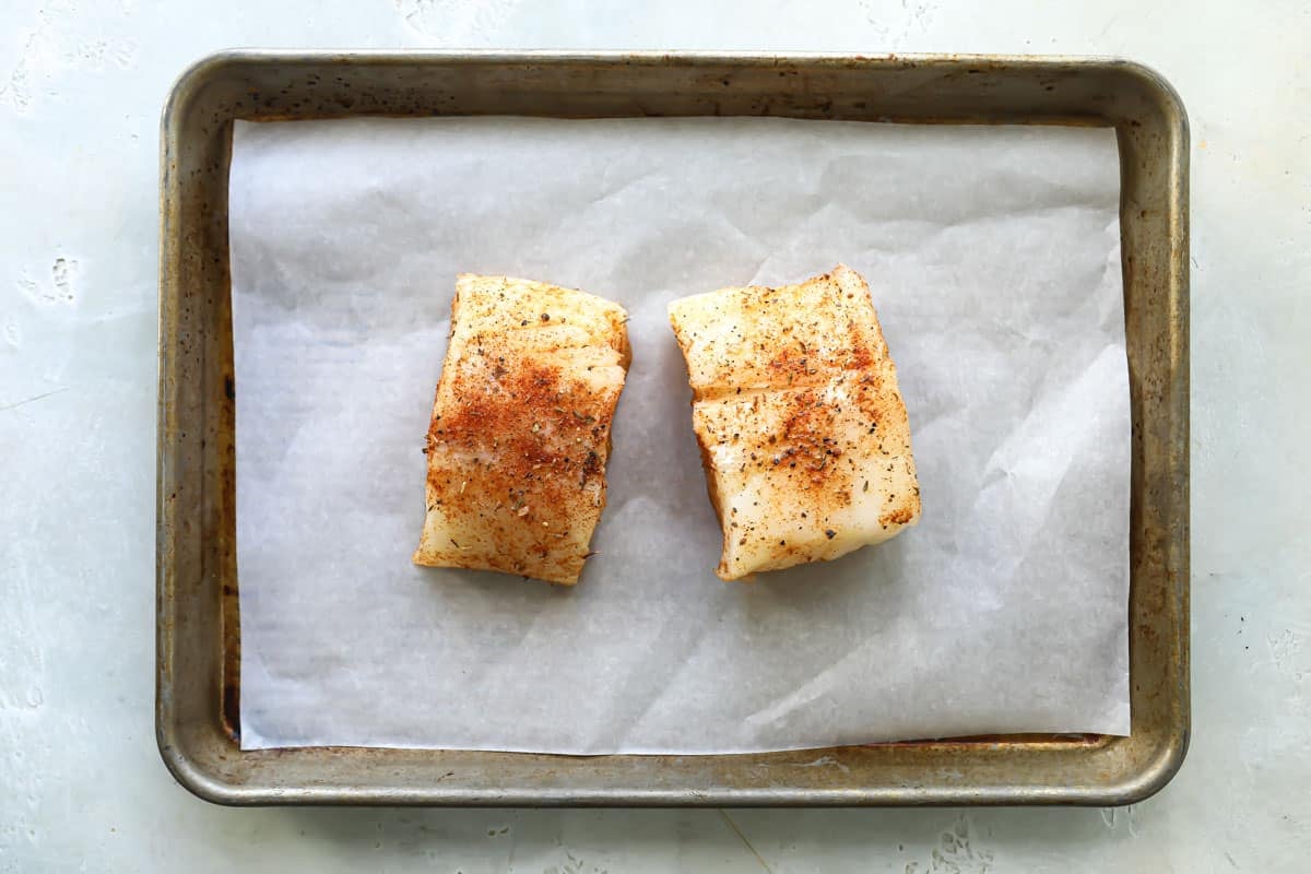 Seasoned cod pieces on a parchment paper lined baking sheet.