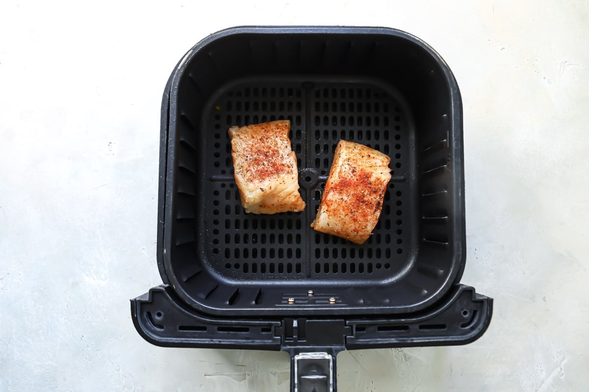Two pieces of seasoned cod in an air fryer basket.