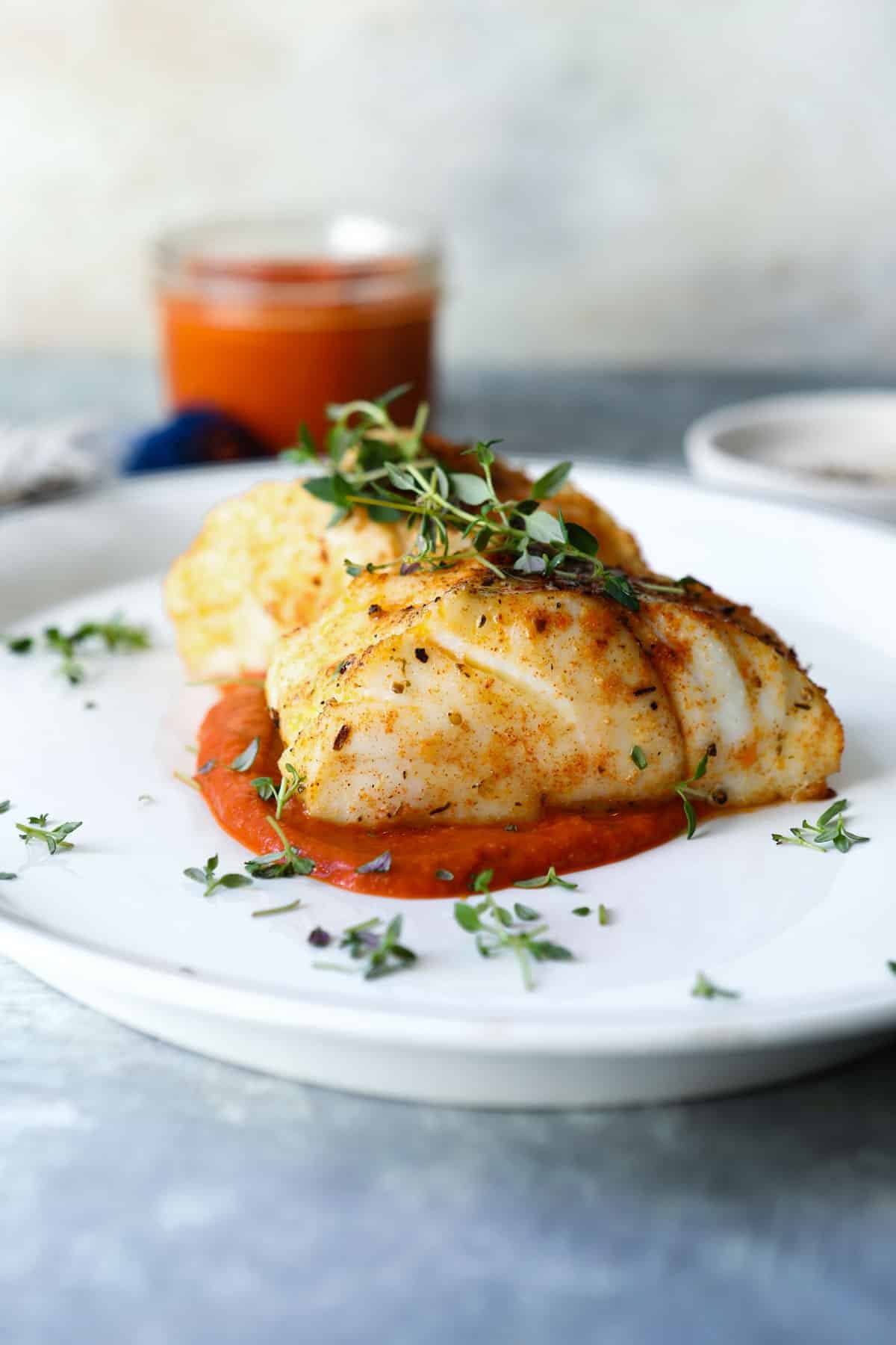 A piece of air fryer cod served over romesco sauce.
