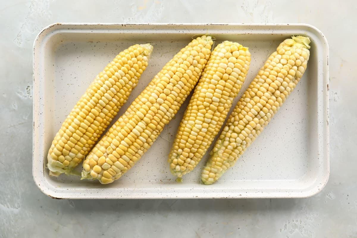 A platter with four uncooked corn on the cob.