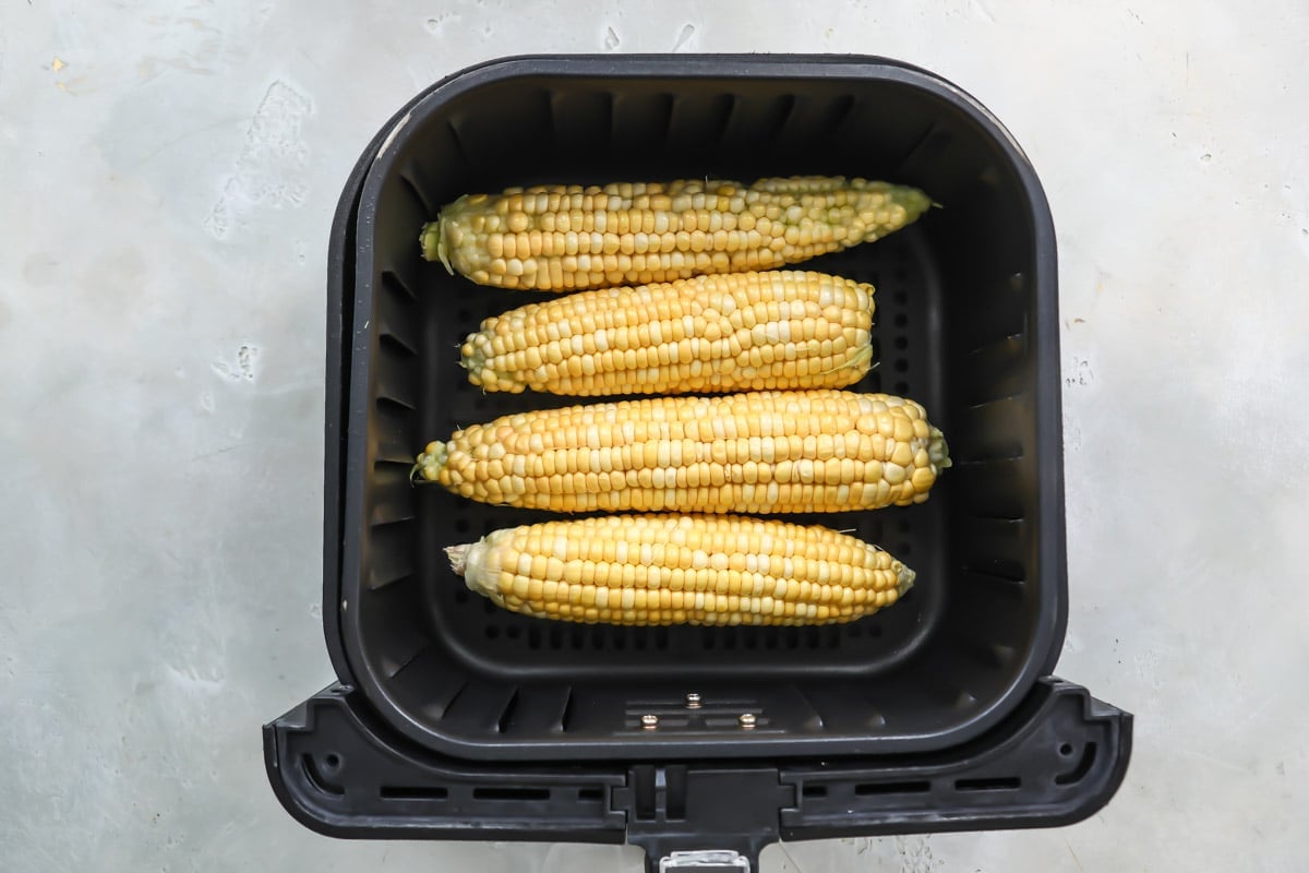 Corn on the cob in an air fryer basket before being cooked.
