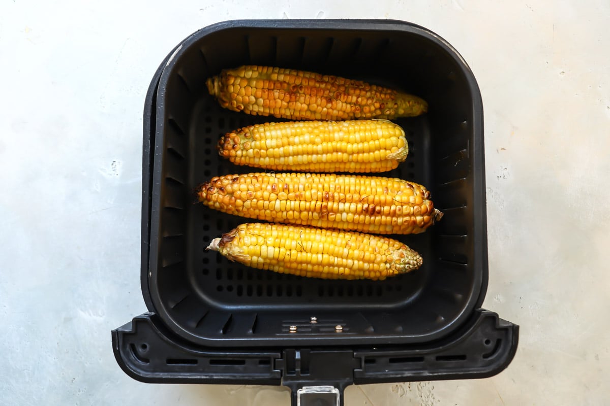An air fryer basket with air fryer corn on the cob in it.