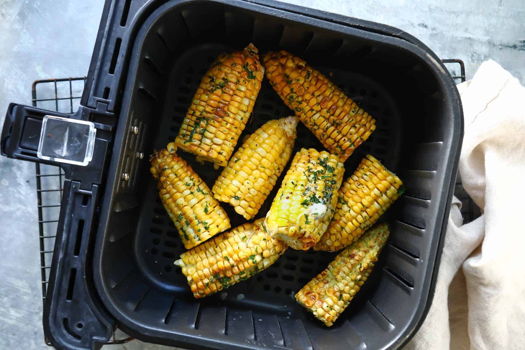 An air fryer basket with cooked cobs of corn in it.