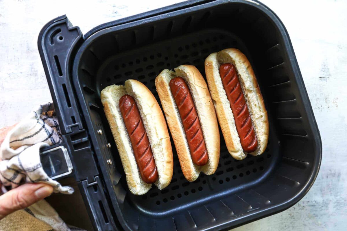 Three hot dogs in buns in an air fryer.