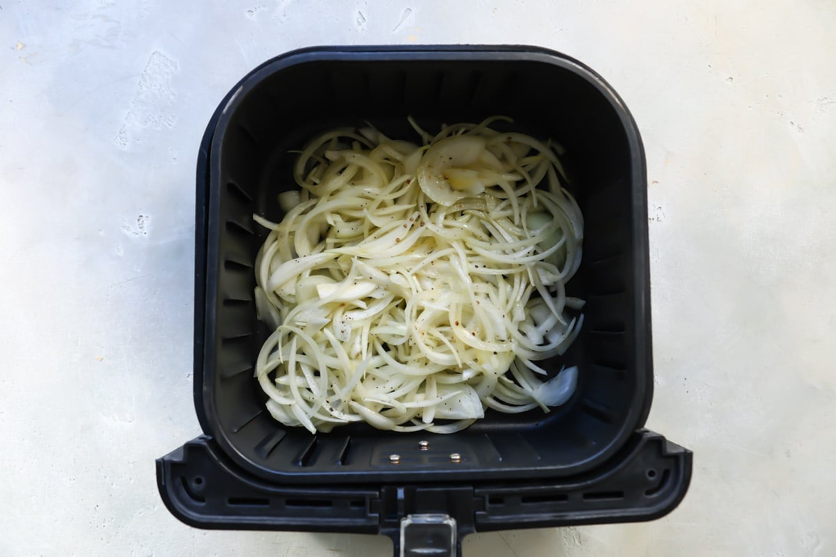 Onions in an air fryer basket before being air fried.