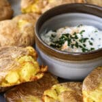 Air fryer smashed potatoes on a platter with a small bowl of white dip in the middle.