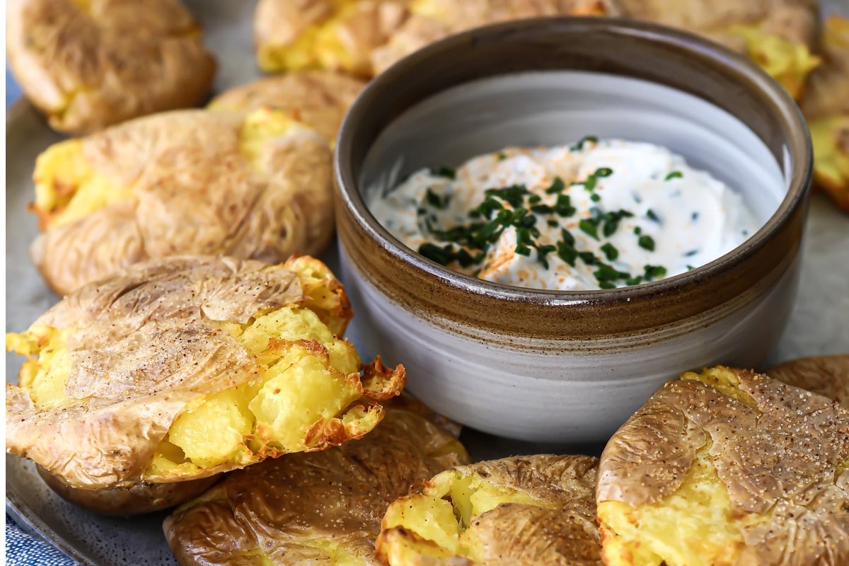 Air fryer smashed potatoes on a platter with a small bowl of white dip in the middle.