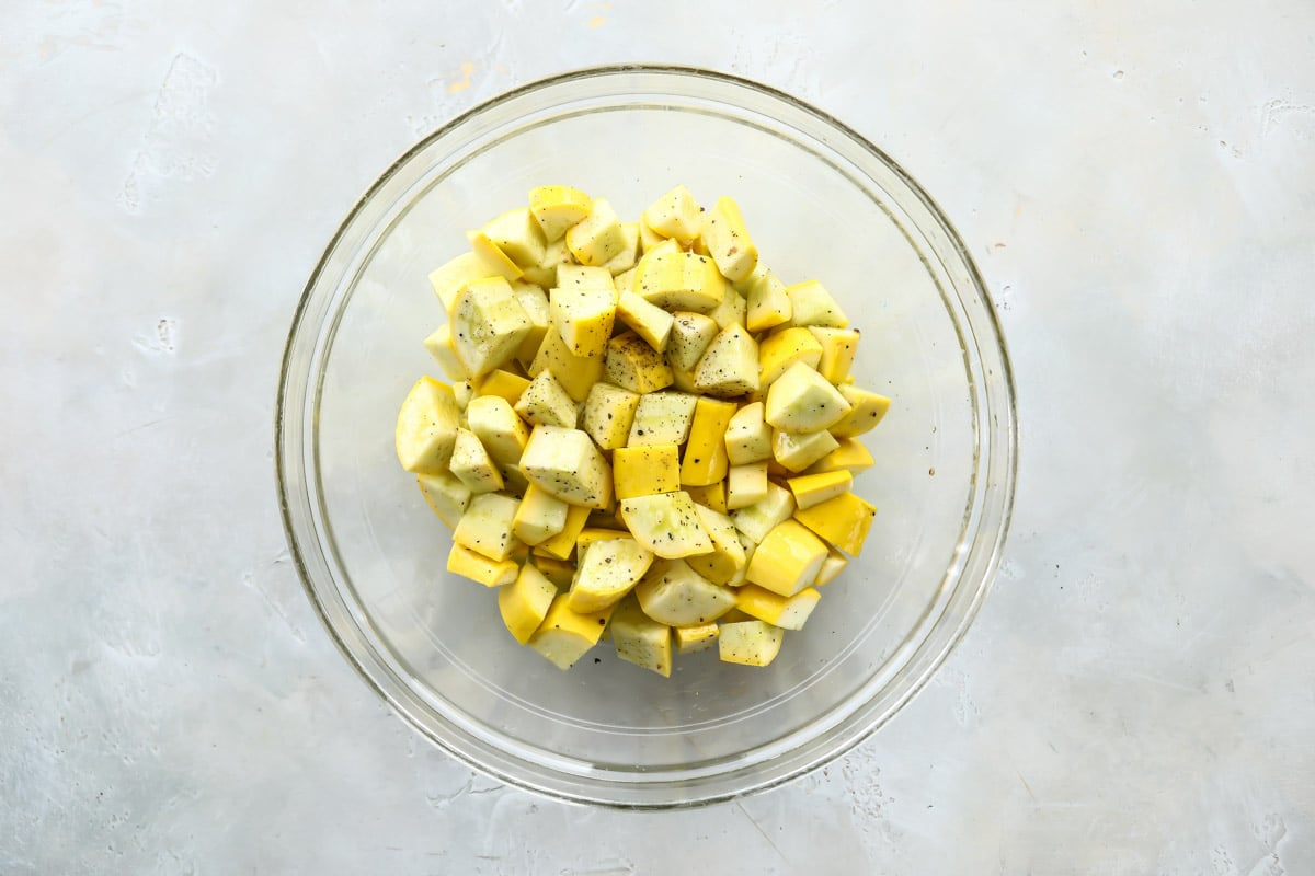 Squash coated in olive oil, salt and pepper in a clear bowl.