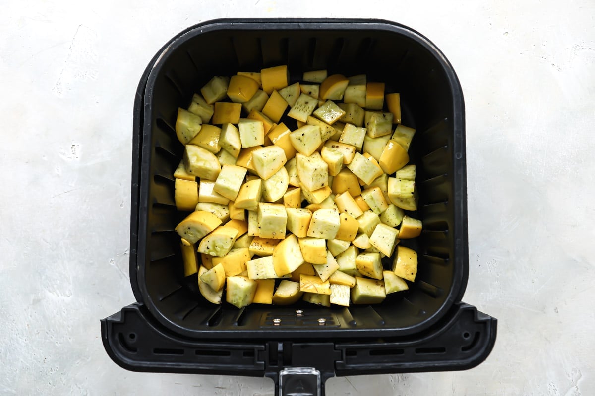Squash in an air fryer basket before being air fried.