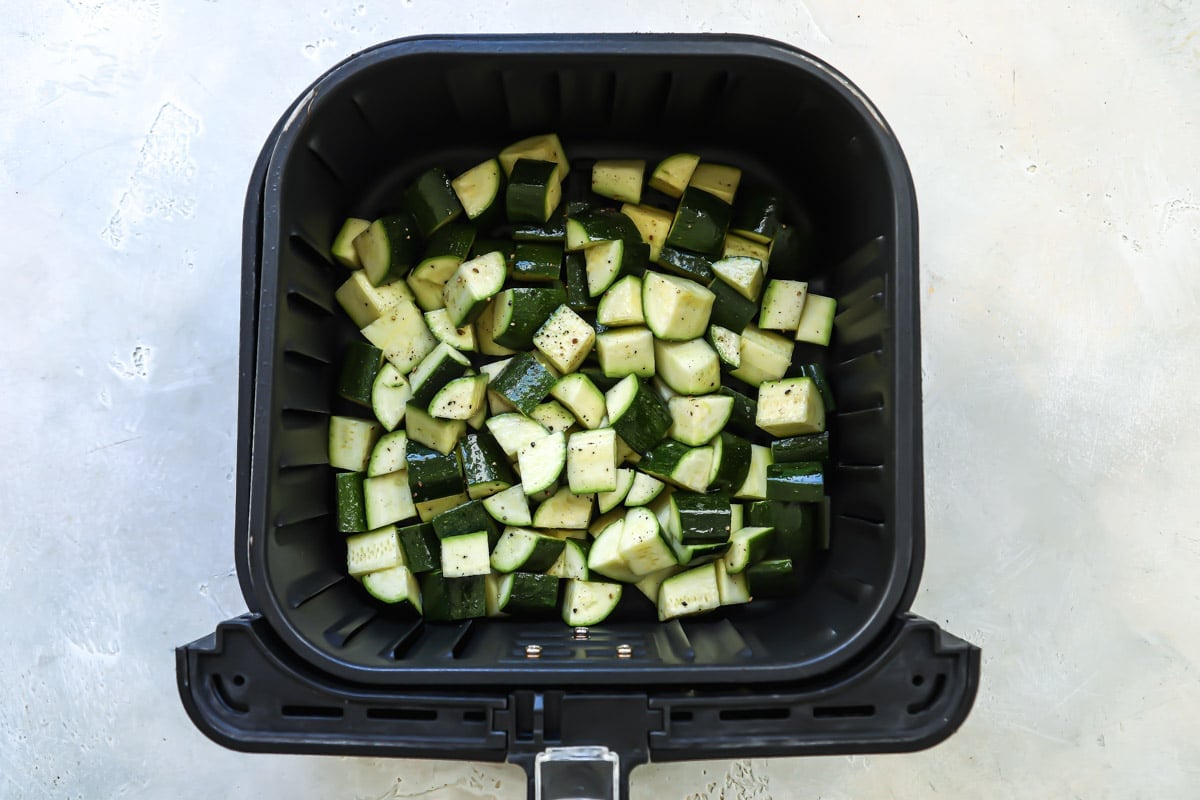 An air fryer basket with raw zucchini in it.