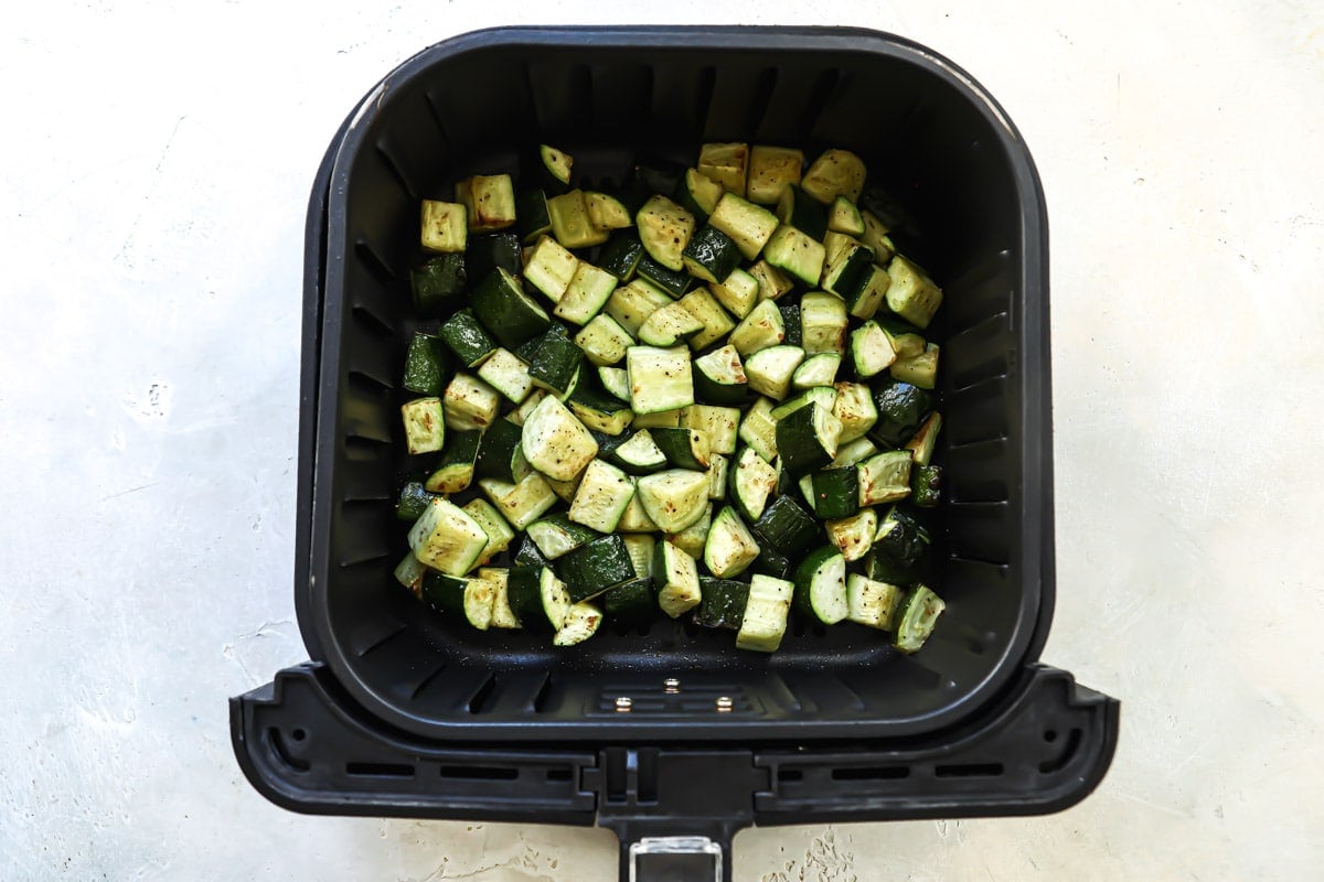 An air fryer basket with air fryer zucchini cubes in it.
