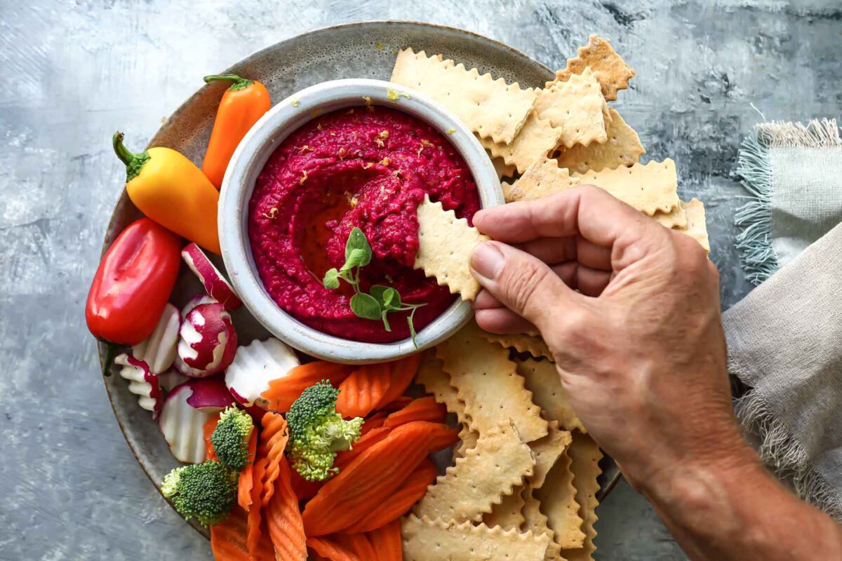 Someone dipping a cracker in beet hummus.