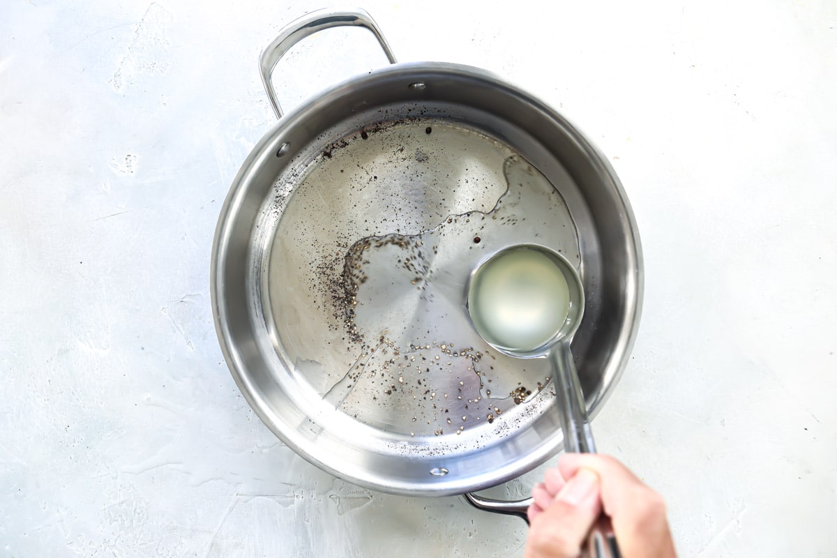 Pasta water being added to a skillet with pepper.