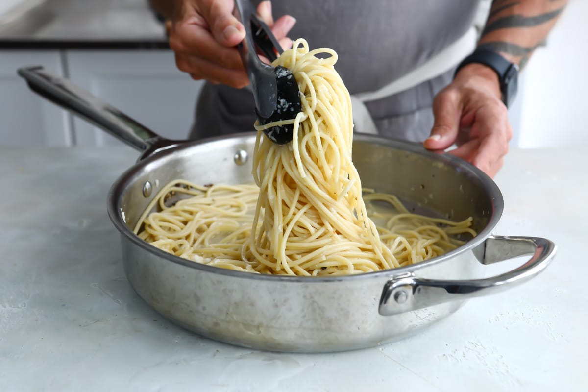 Someone tossing cacio e pepe with tongs over a silver skillet.