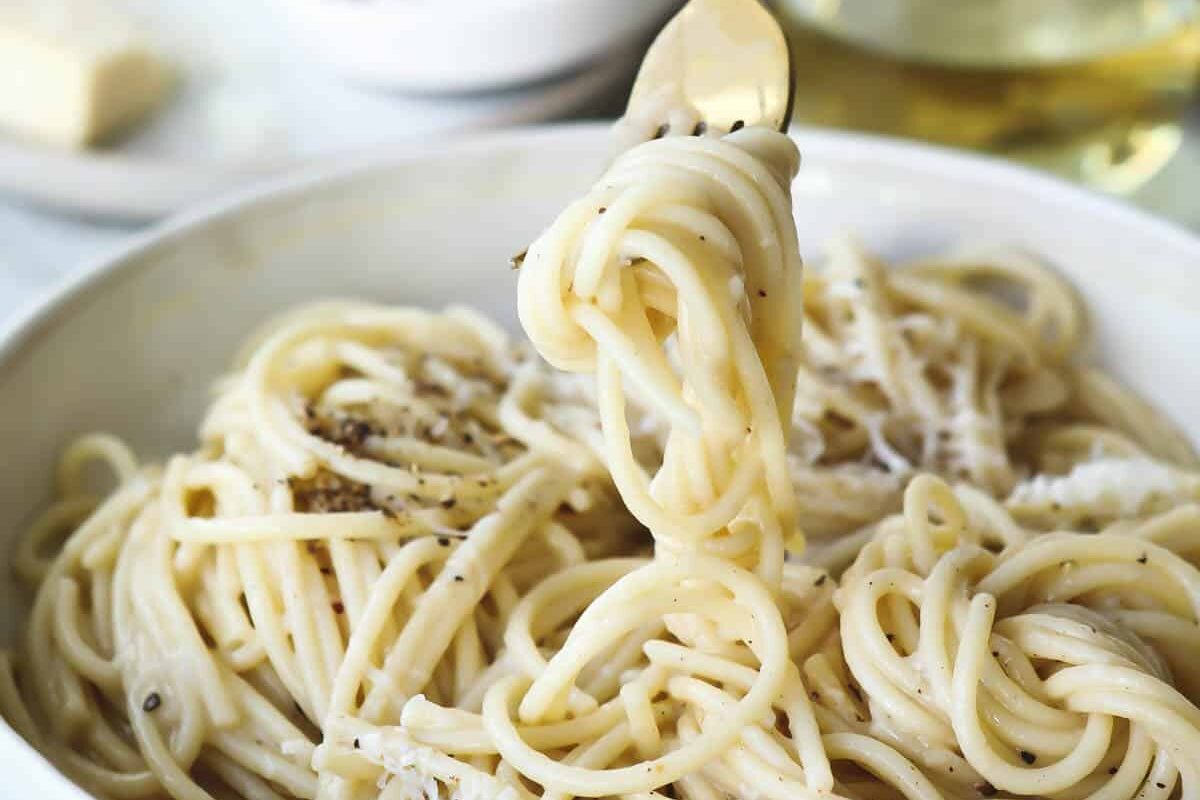 Someone taking a fork of Cacio e pepe out of a white bowl.
