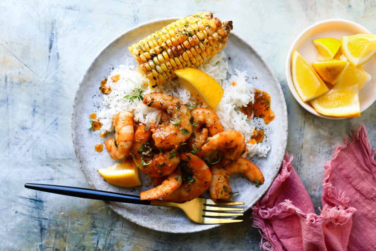 Cajun shrimp on a plate with rice and corn on the cob.