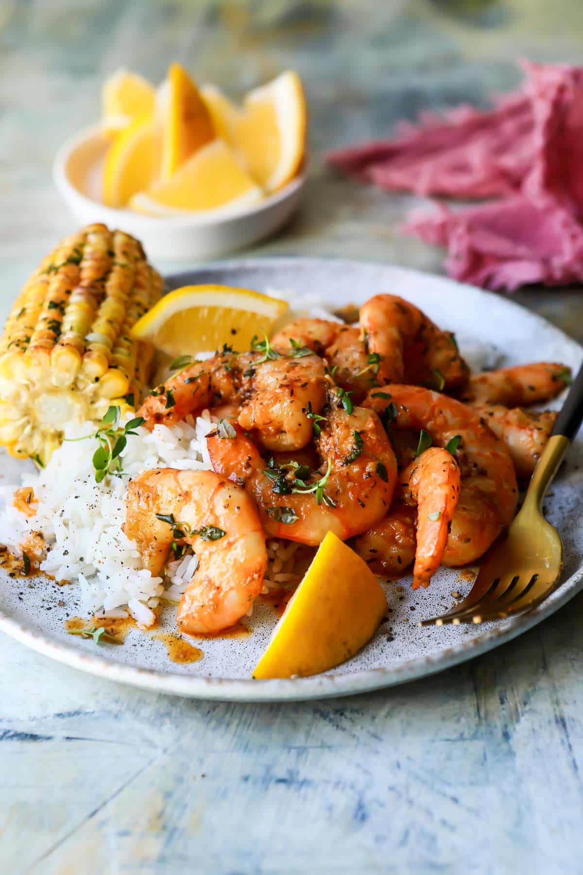 Cajun shrimp on a plate with corn, rice, and lemons wedges.
