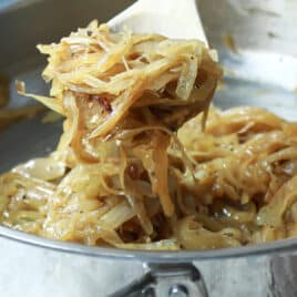 Someone scooping out a spoonful of caramelized onions out of a metal skillet.