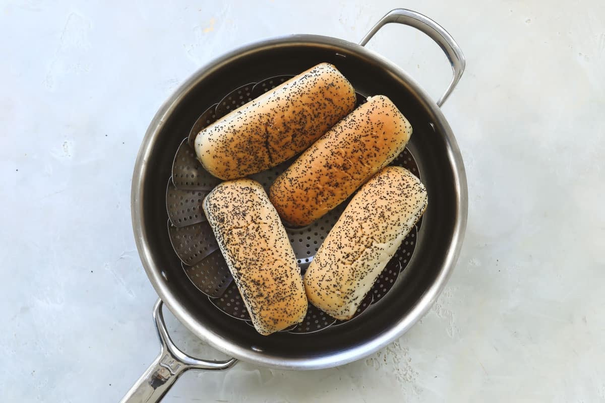 Four hot dog buns in a steamer basket.