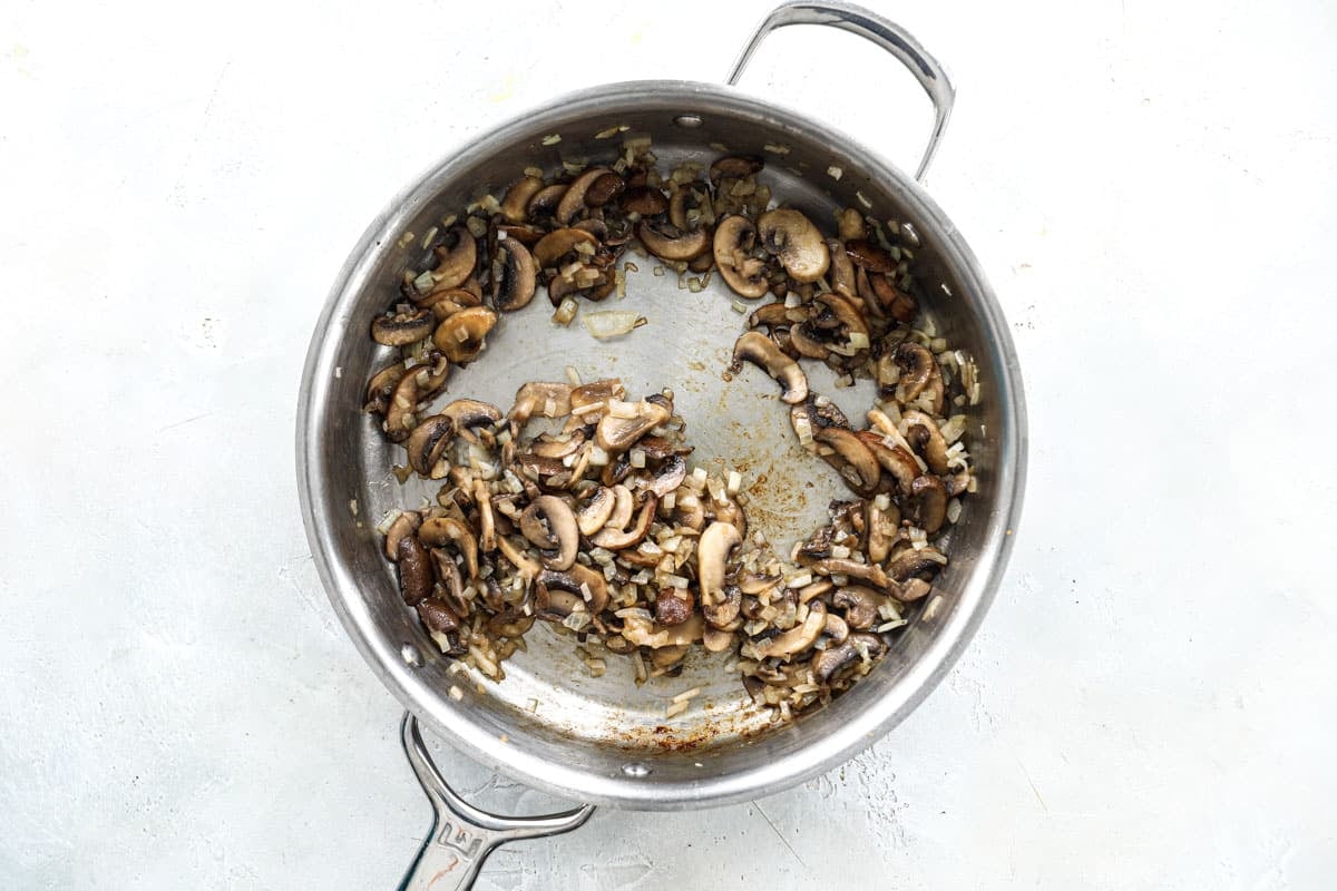 Mushrooms, onions, and spices being cooked in a silver skillet for mushroom gravy.