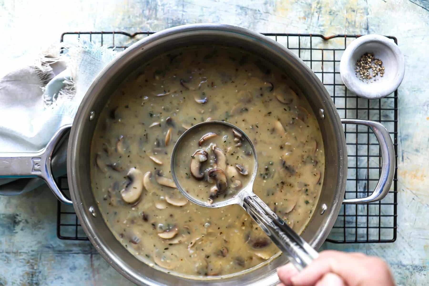 Someone holding a ladle of mushroom gravy over a pot of mushroom gravy.
