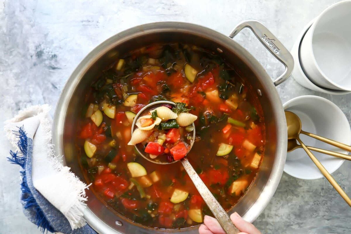 Someone ladling a scoop of minestrone out of a pot.