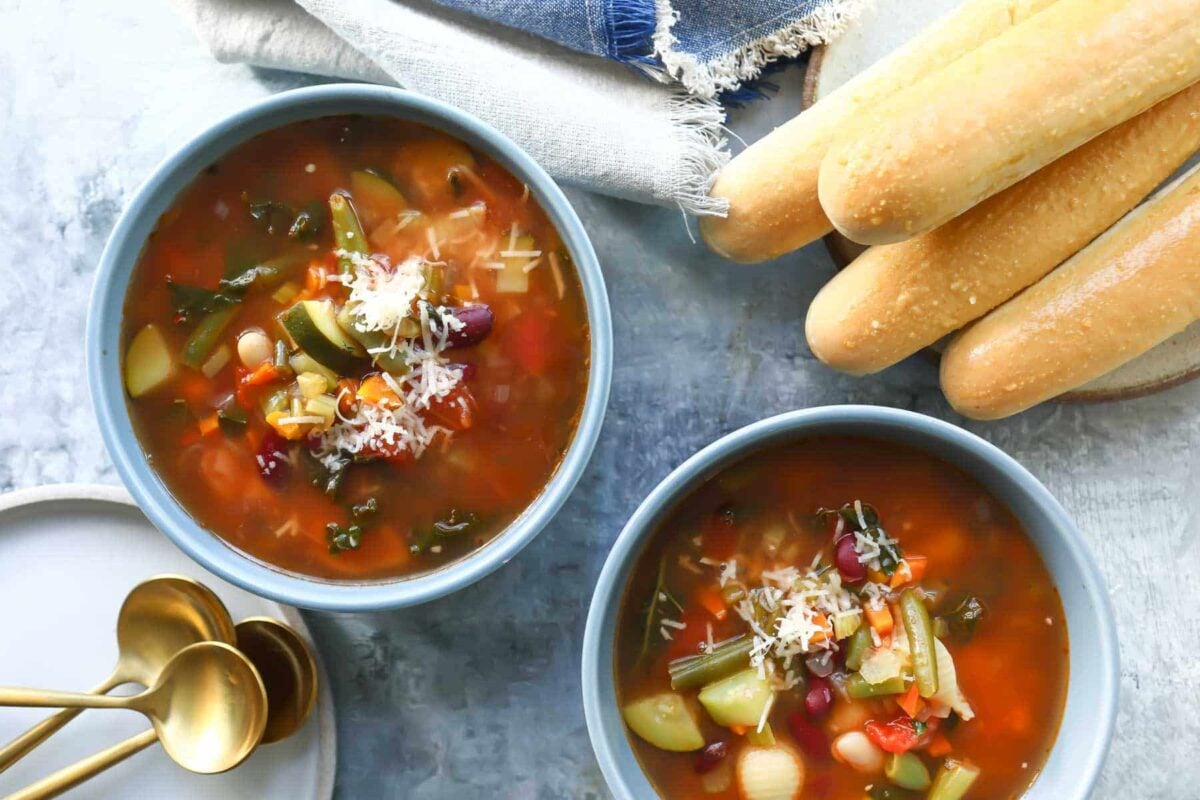 Two bowls of Olive Garden Minestrone soup next to breadsticks.