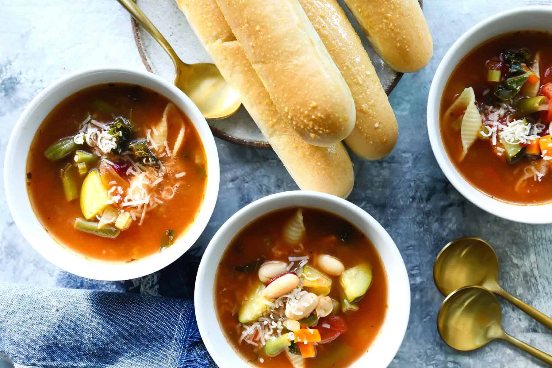 Three bowls of Copycat Olive Garden Minestrone next to breadsticks.