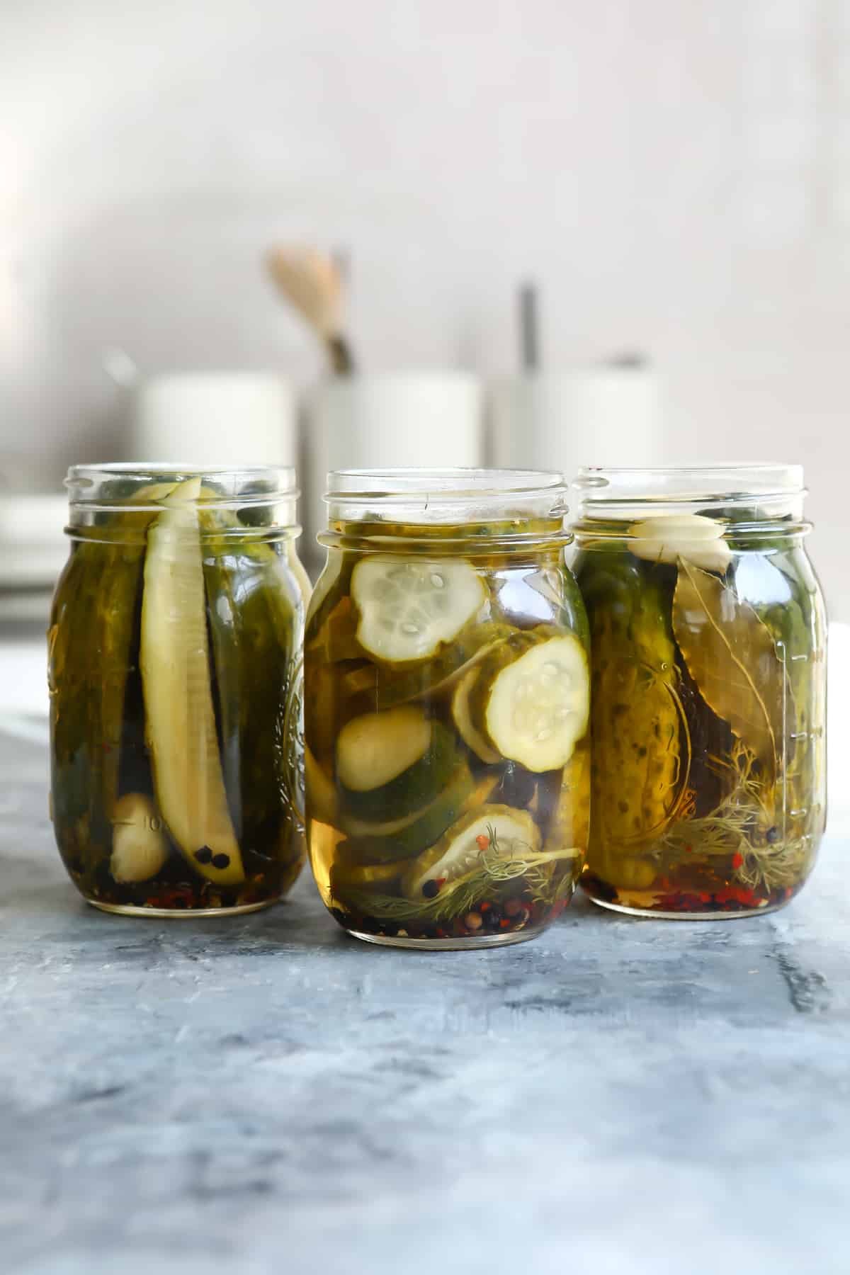 Three jars of pickles on a countertop.