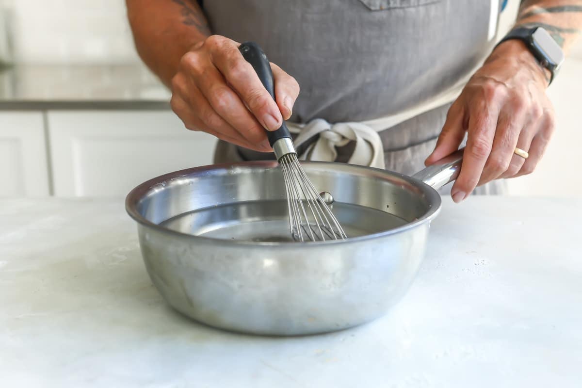 Someone mixing a clear liquid with a whisk in a silver saucepan.