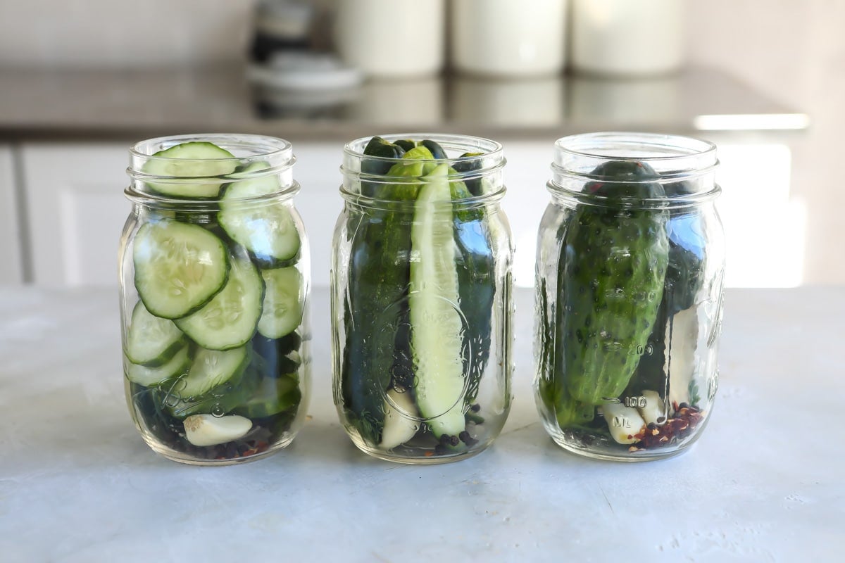 Three jars with cucumbers and spices in them.