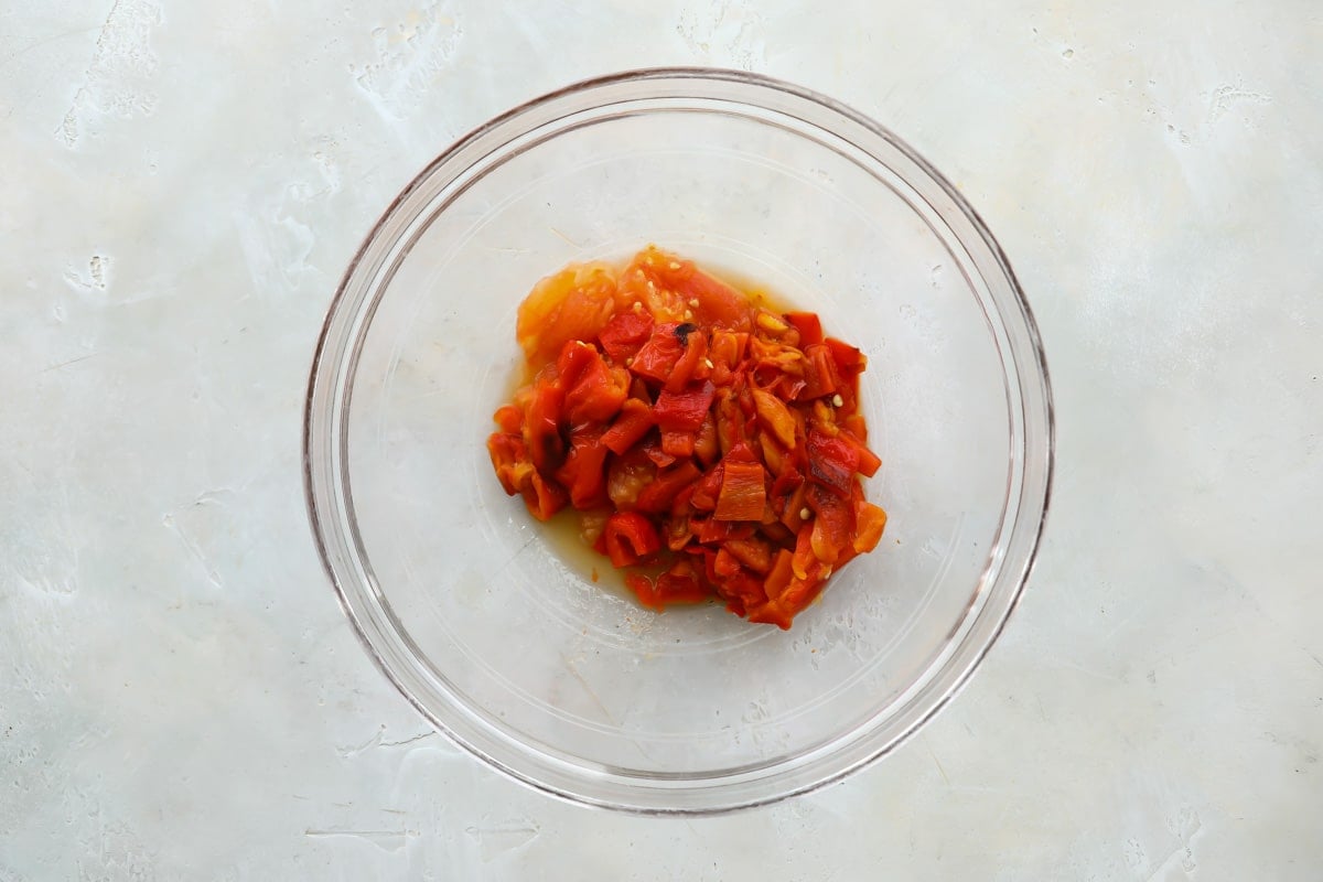 Cut up roasted red pepper and tomato in a clear bowl.