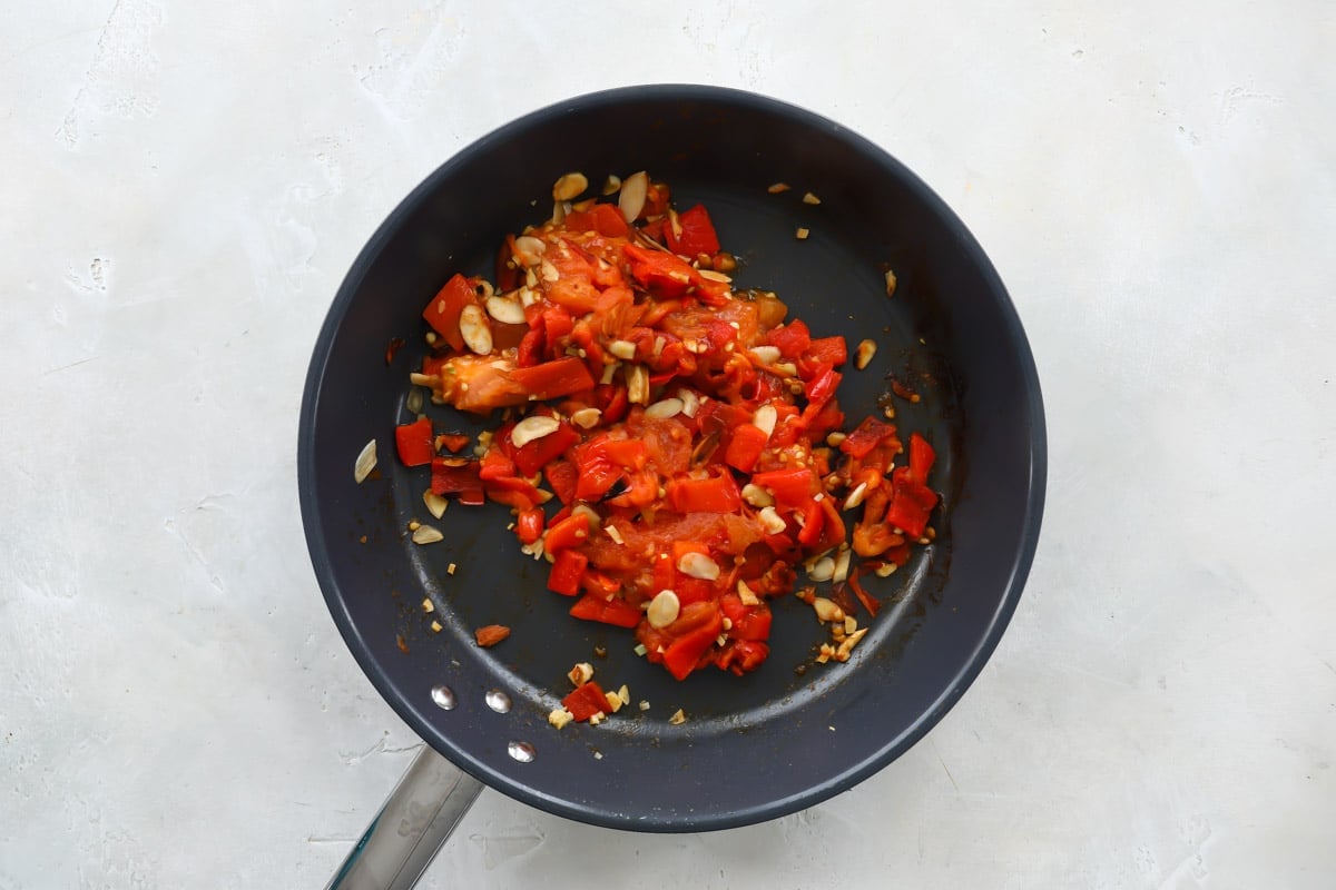 Ingredients for Romesco sauce cooking in a black skillet.