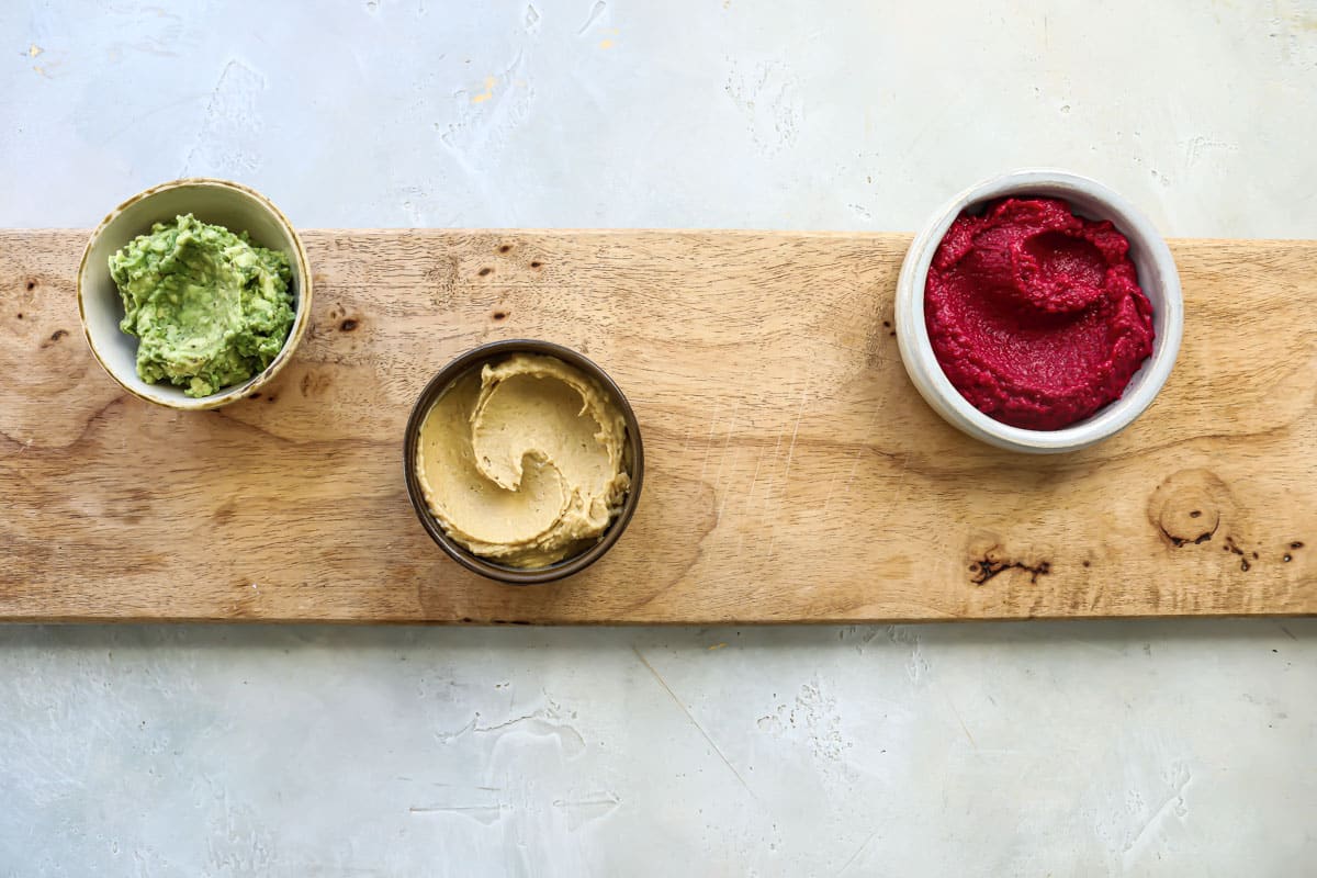 Three vegan dips on a wooden board for a vegan charcuterie board.
