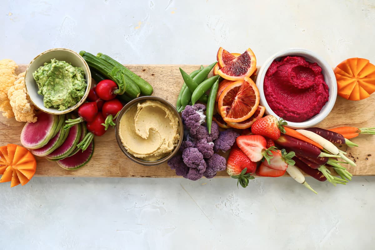 Dips, fruits and veggies on a wooden board for a vegan charcuterie board.
