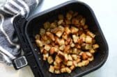 An air fryer basket with croutons in it.