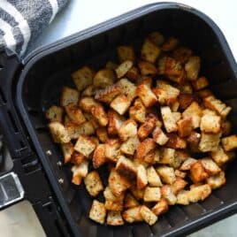 An air fryer basket with croutons in it.