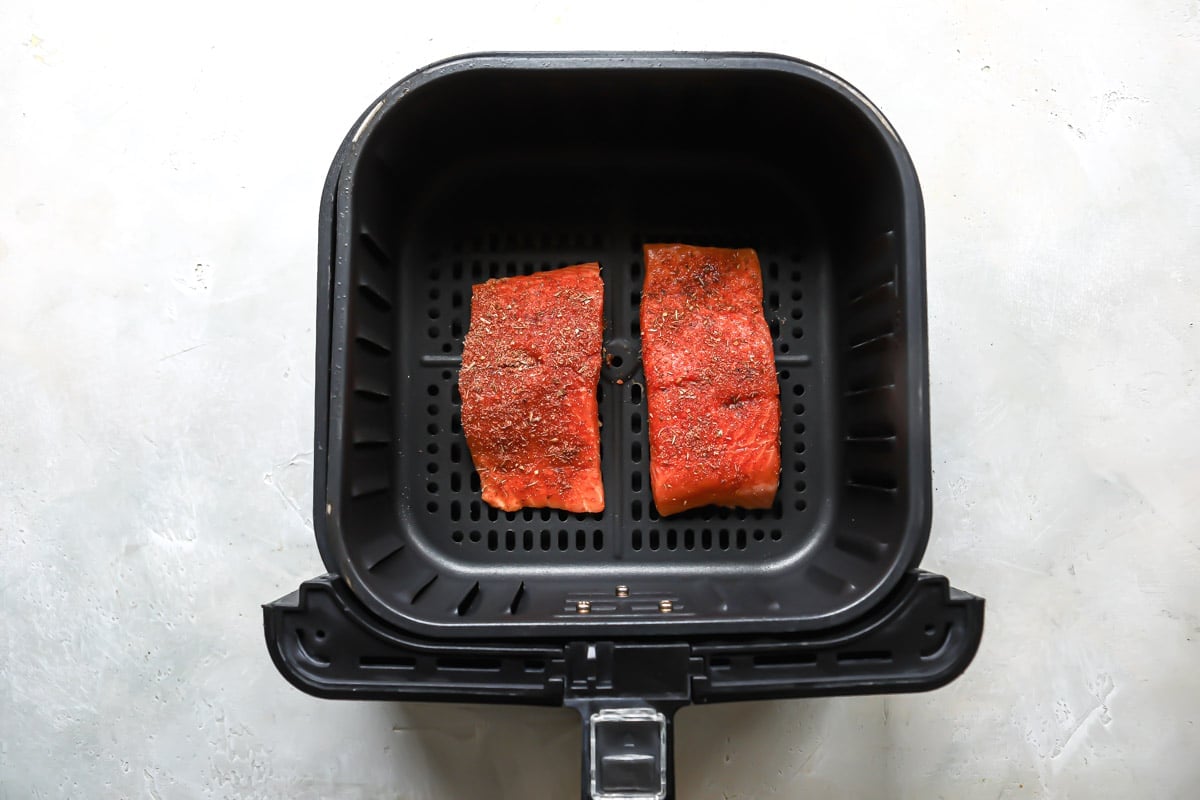Two pieces of seasoned salmon in an air fryer basket before being air fried.