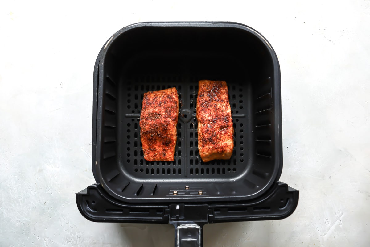 Two pieces of air fryer salmon in an air fryer basket.