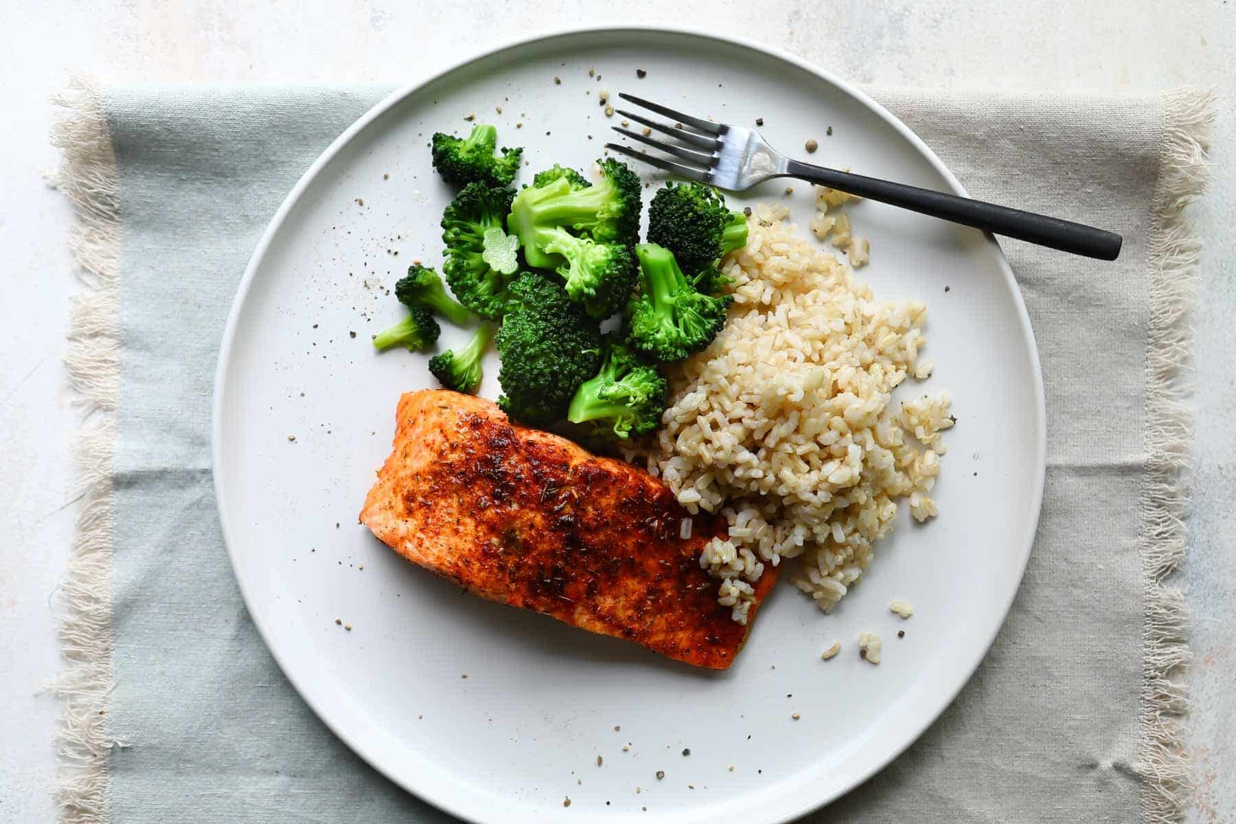 A plate with salmon, rice and broccoli.