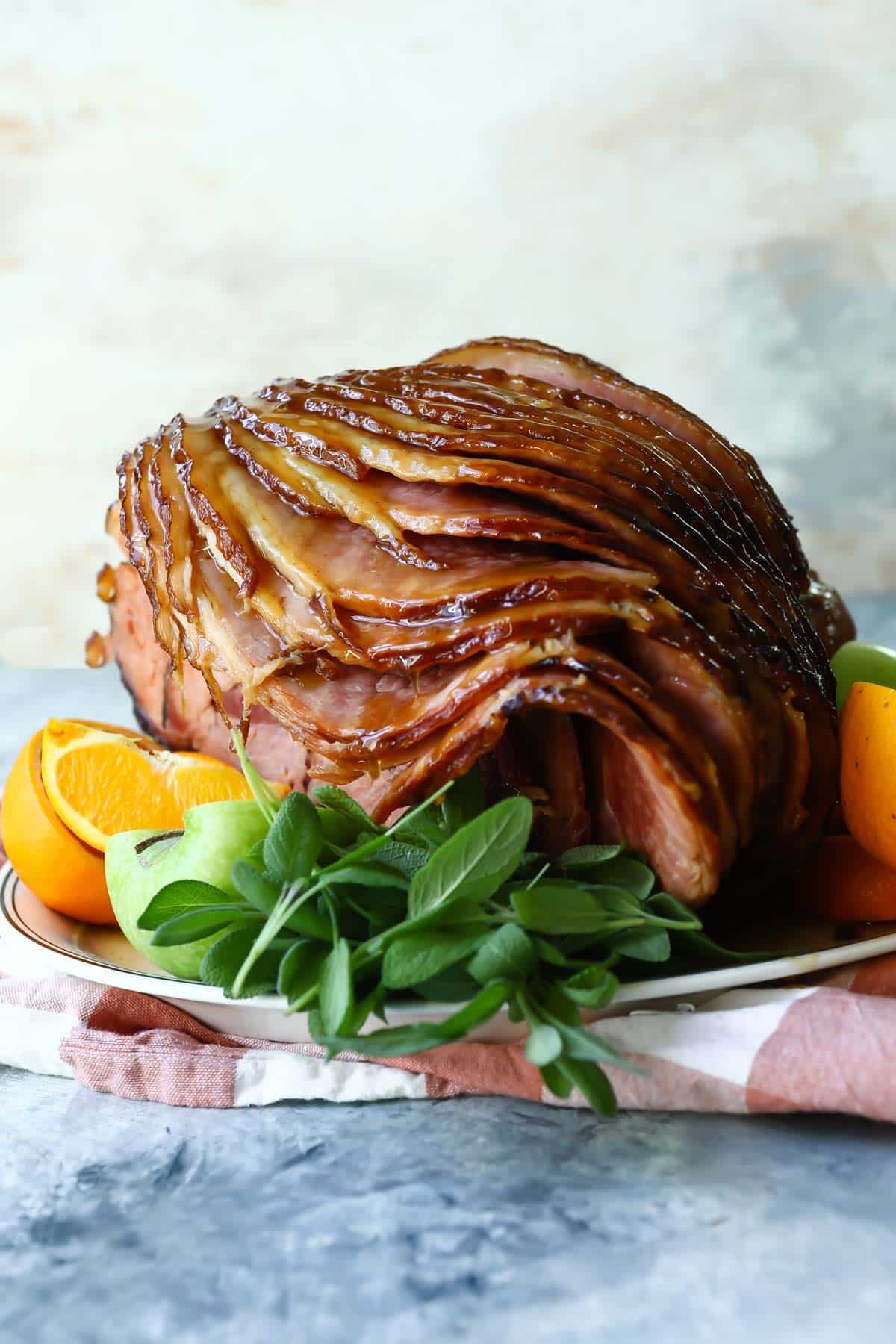 A sliced baked ham on a platter with fresh herbs and oranges.