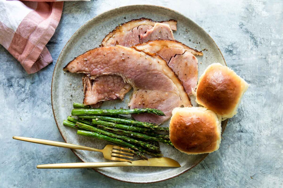 A plate of baked ham, air fryer asparagus, and soft yeast rolls.