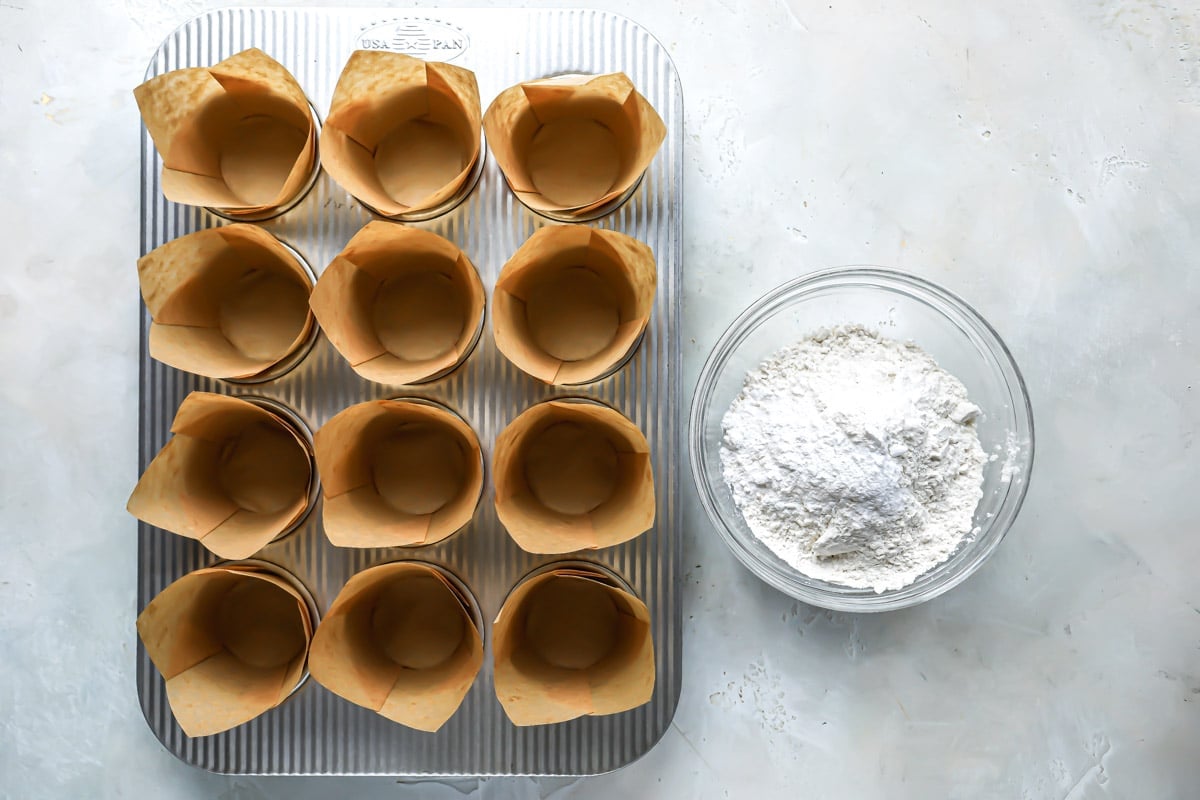 A muffin pan with liners next to a bowl of dry ingredients.