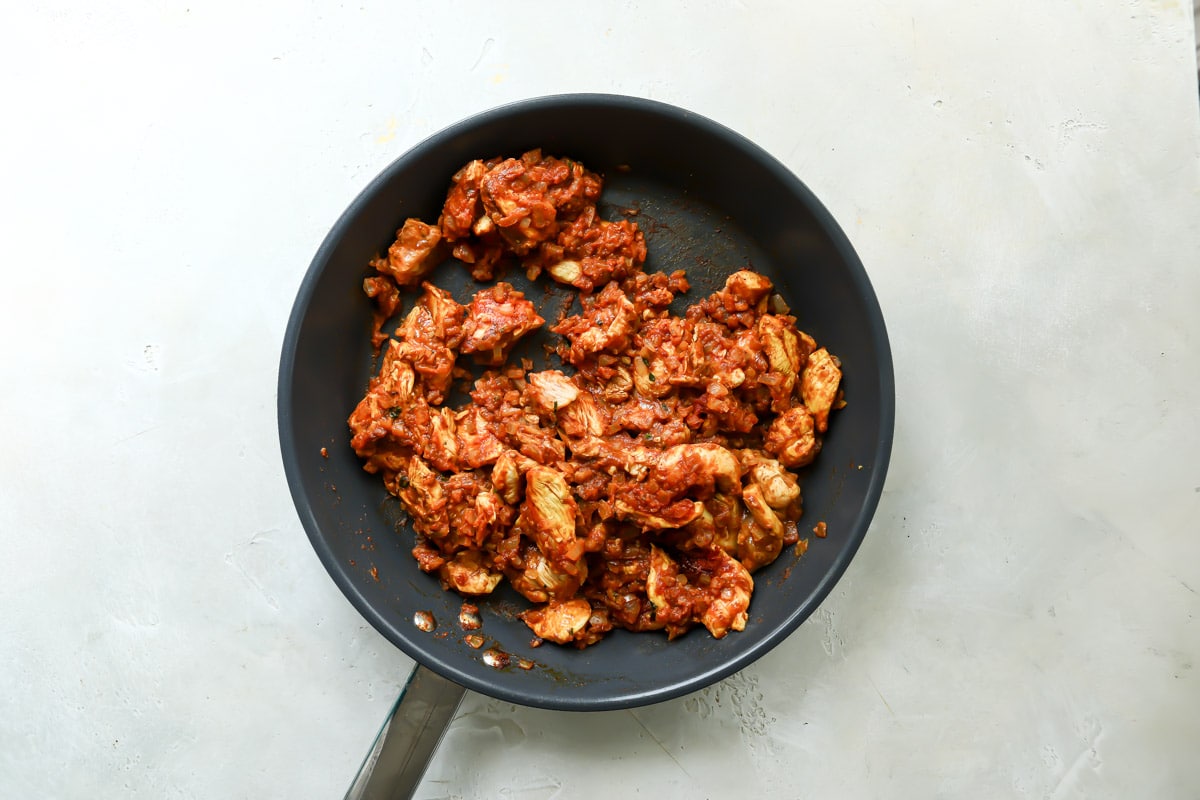 Chicken and spices in a skillet to make butter chicken.
