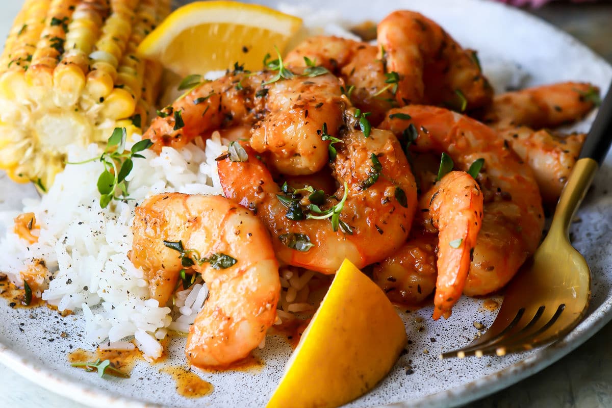 A plate of cajun shrimp, white rice, and corn on the cob.